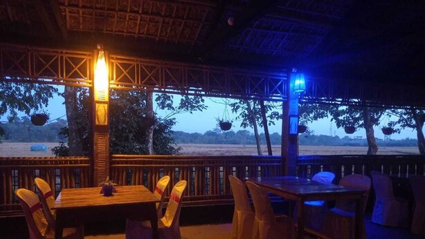 An outdoor dining area with a table and chairs, a hanging light fixture, and a view of the beach. - Pobitora Village Eco Camp (Mayang)