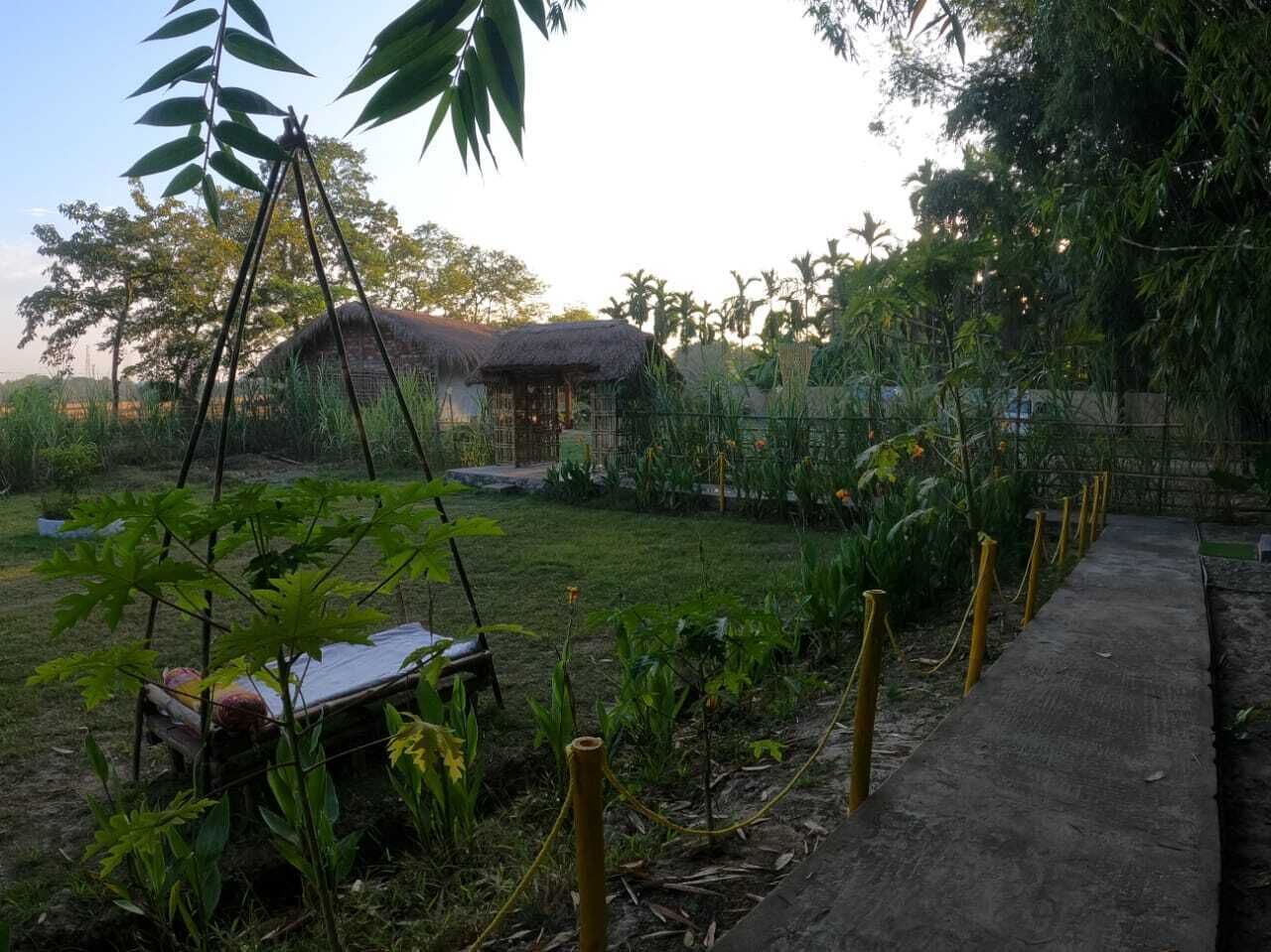 A garden with a thatched-roof structure, a swing set, and a concrete pathway.