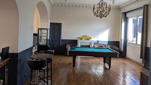 A billiards room with a pool table, bar stools, a chandelier, and a toy car on a cabinet. - Hôtel Le Millésime (Meymac)
