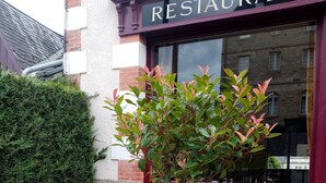 An outdoor seating area with a table and chairs, a small tree, and a building with a 'RESTAURANT' sign. - Hôtel Le Millésime (Meymac)