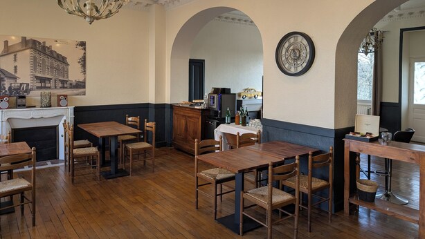 A dining area with wooden tables and chairs, a chandelier, a vintage clock, and a fireplace. - Hôtel Le Millésime (Meymac)