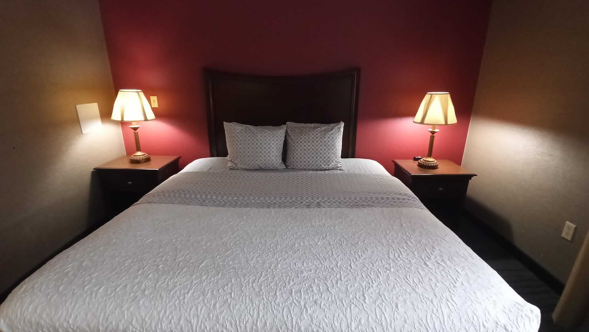 A neatly made bed with a white duvet, two pillows, and two bedside lamps on wooden nightstands.