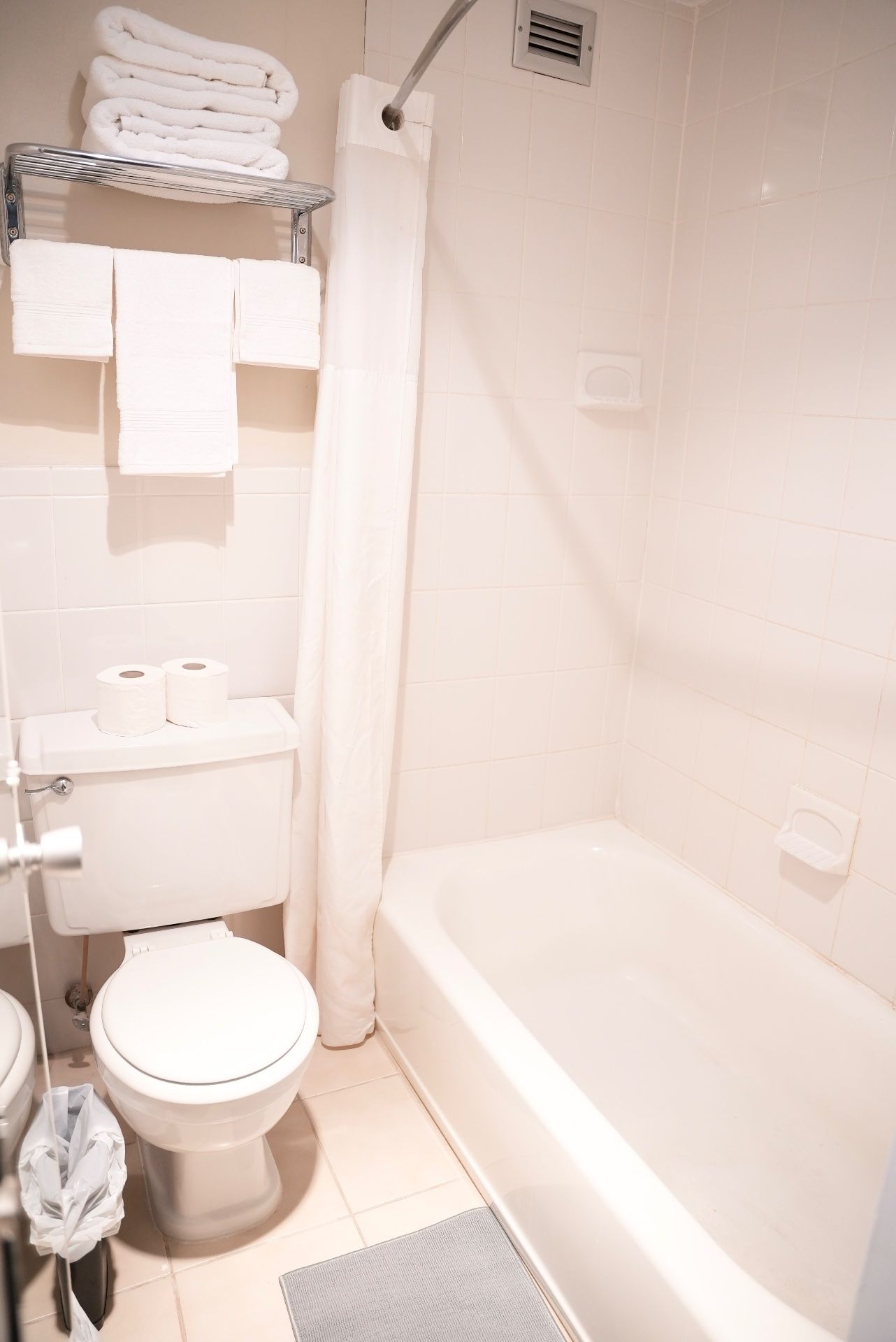 Un baño con inodoro, bañera, cortina de ducha y toallero con toallas dobladas.