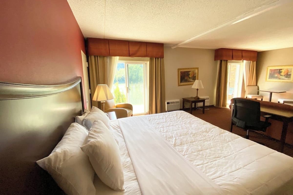 A hotel room with a large bed, a desk, a chair, and a painting on the wall.
