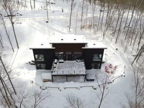 A modern two-story house surrounded by snow-covered trees.