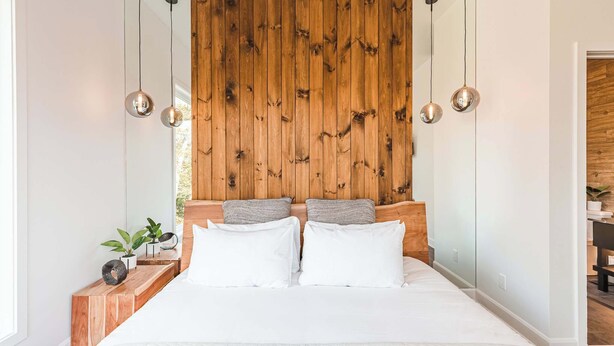 Ein Schlafzimmer mit hölzernem Kopfteil, einem Bett mit weißer Bettwäsche, zwei Nachttischen mit Pflanzen und Pendelleuchten.