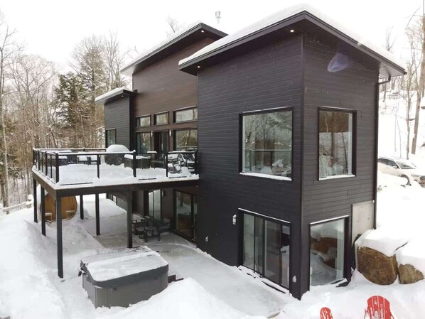 A modern two-story house with a balcony, large windows, and a snow-covered exterior.