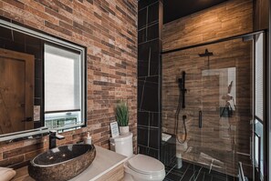 A modern bathroom with a brick wall, a large mirror, a freestanding sink, and a glass shower enclosure.