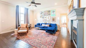 A spacious living room with a blue sofa, a patterned rug, and a fireplace. - Modern 3BR Retreat • EV Charger • Fenced Yard by XNA (Cave Springs)