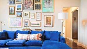 A living room with a blue sectional sofa, framed artwork on the wall, and a lamp. - Modern 3BR Retreat • EV Charger • Fenced Yard by XNA (Cave Springs)