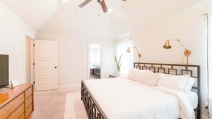 A bedroom with a bed, dresser, ceiling fan, bedside lamps, and a door. - Modern 3BR Retreat • EV Charger • Fenced Yard by XNA (Cave Springs)