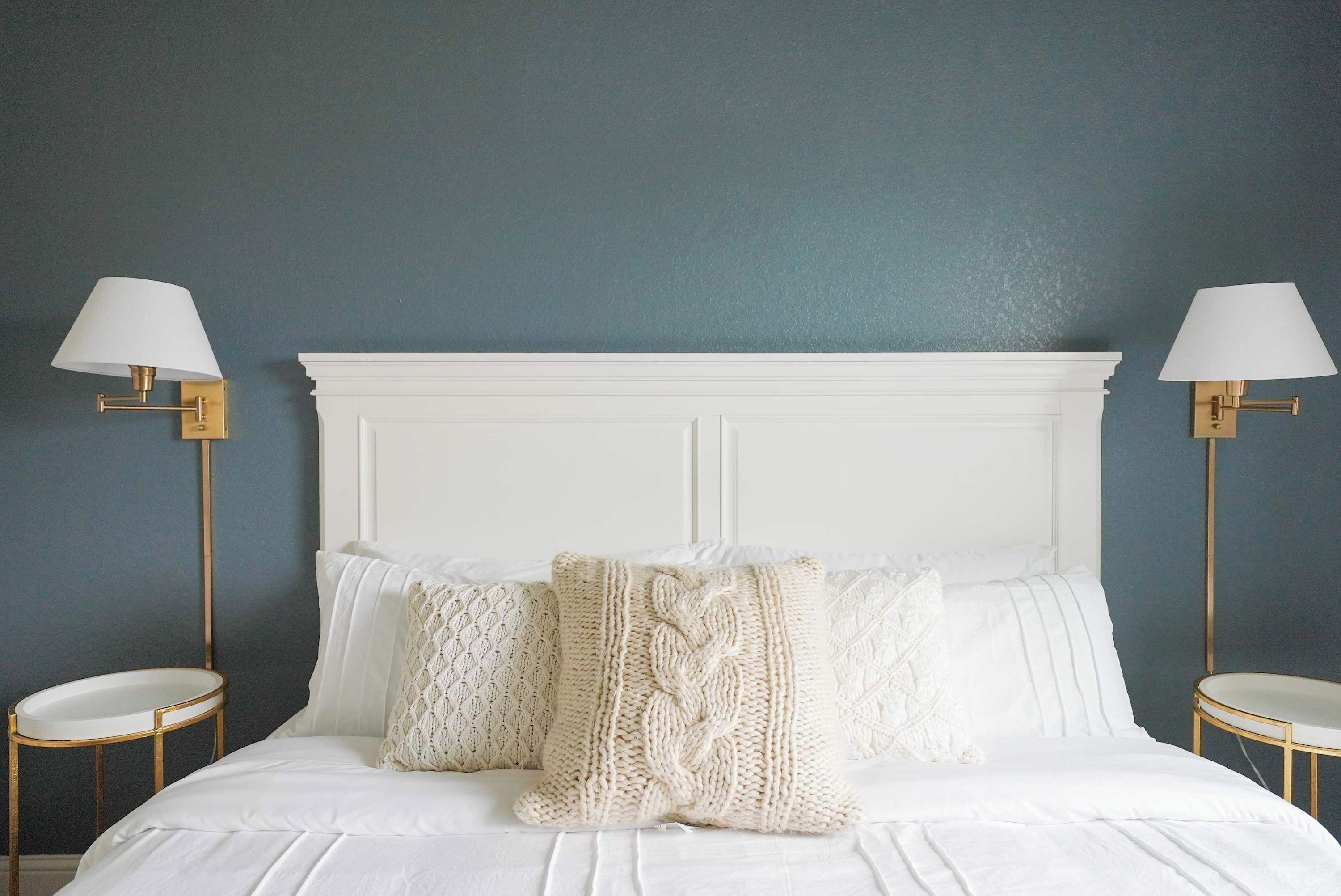 A bed with a white headboard, two bedside tables with gold frames, and two wall-mounted lamps with white shades.