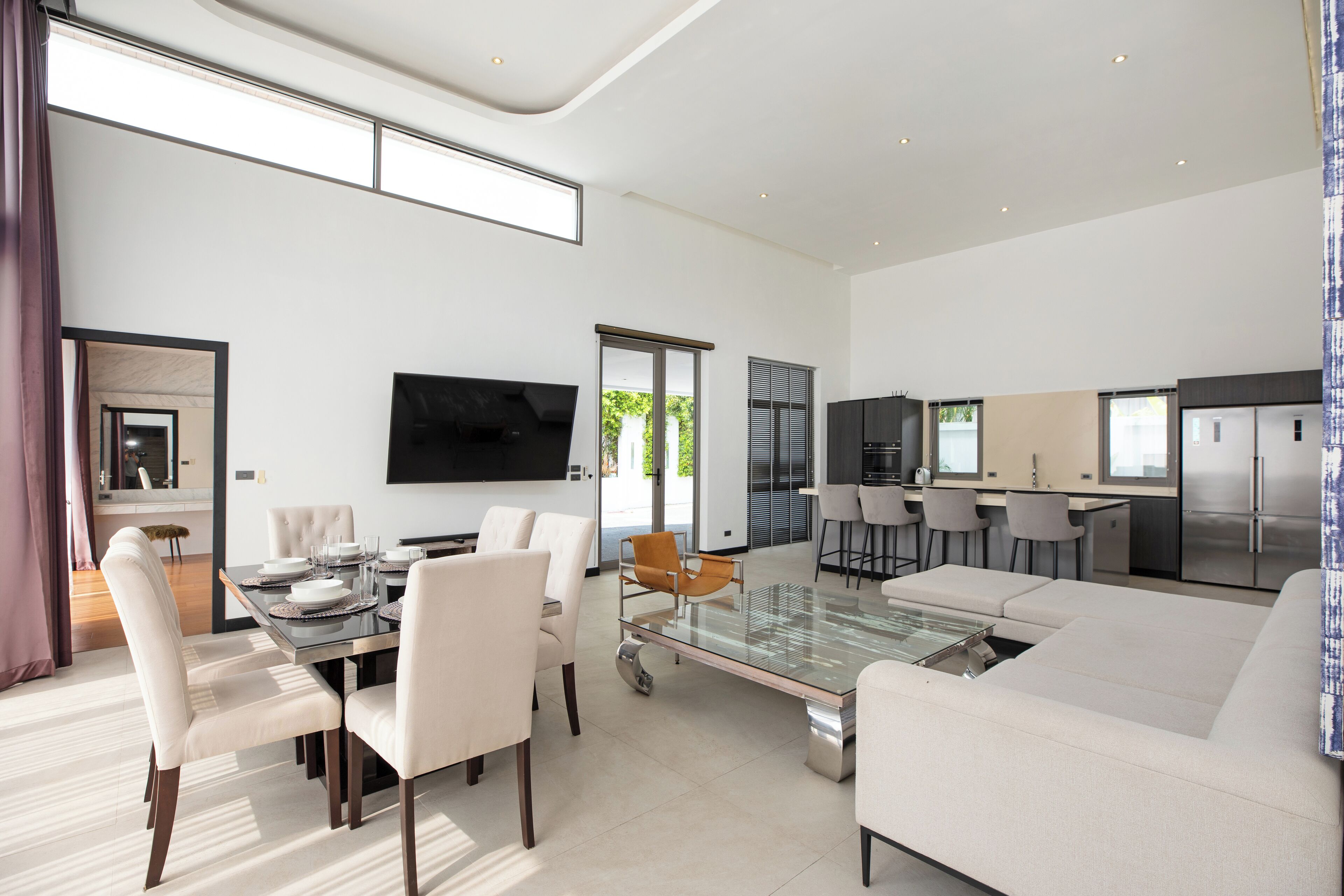 Een moderne woonkamer met een glazen salontafel, witte banken en een eethoek met een tafel gedekt voor vier personen.