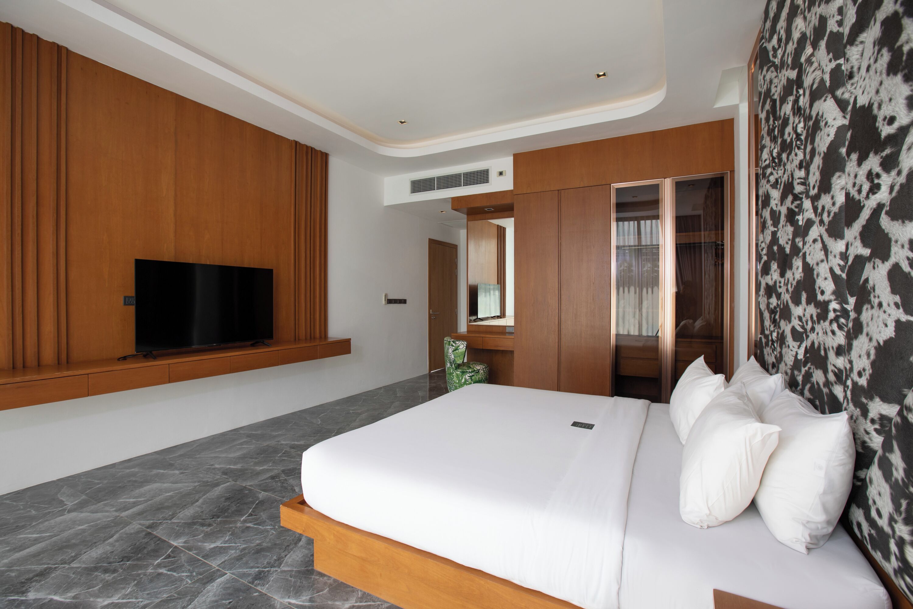 Una habitación de hotel moderna con una cama grande, un televisor de pantalla plana, paneles de madera, un armario y una cortina estampada.