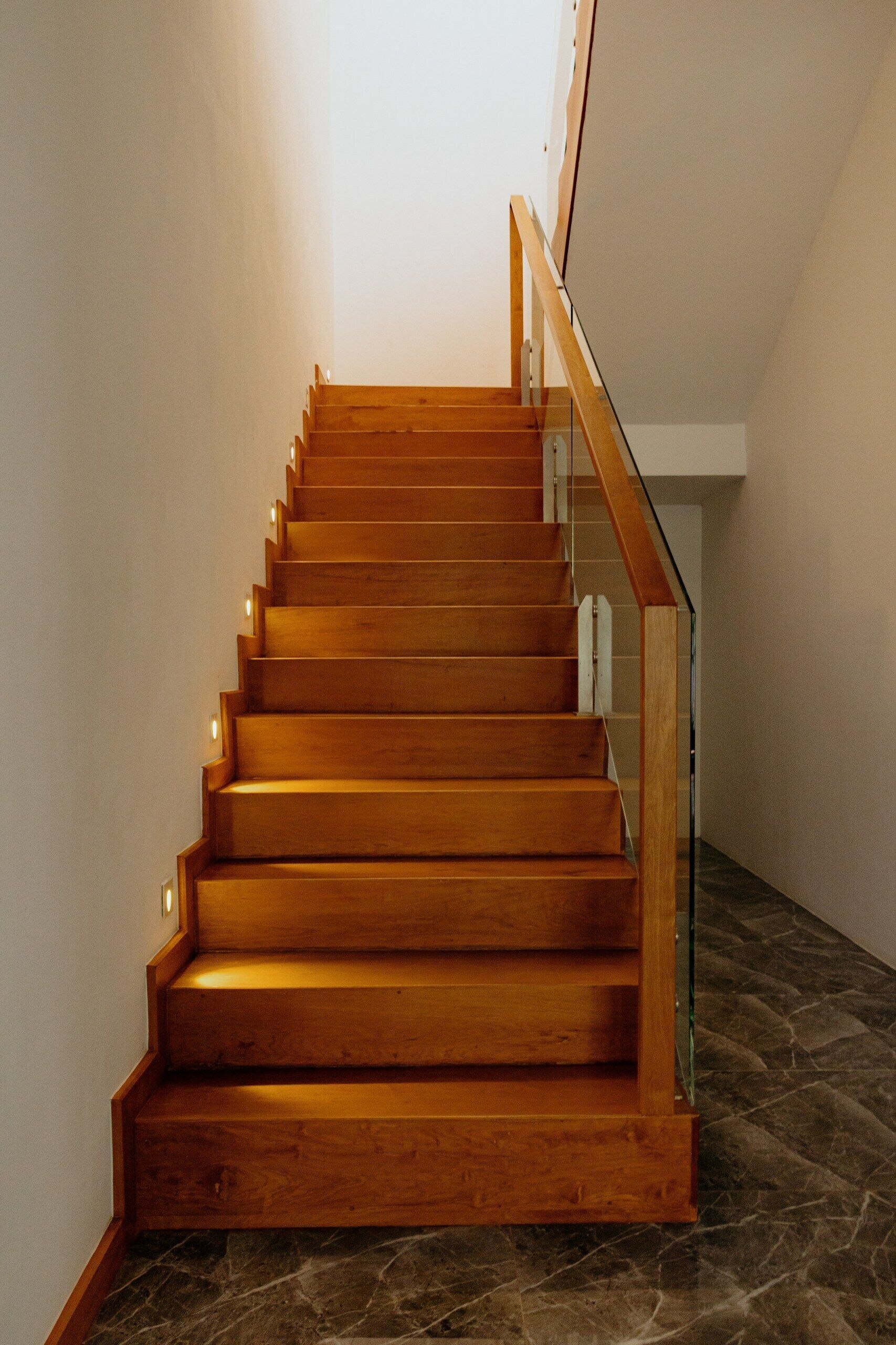 A wooden staircase with a glass railing, leading to an upper floor.