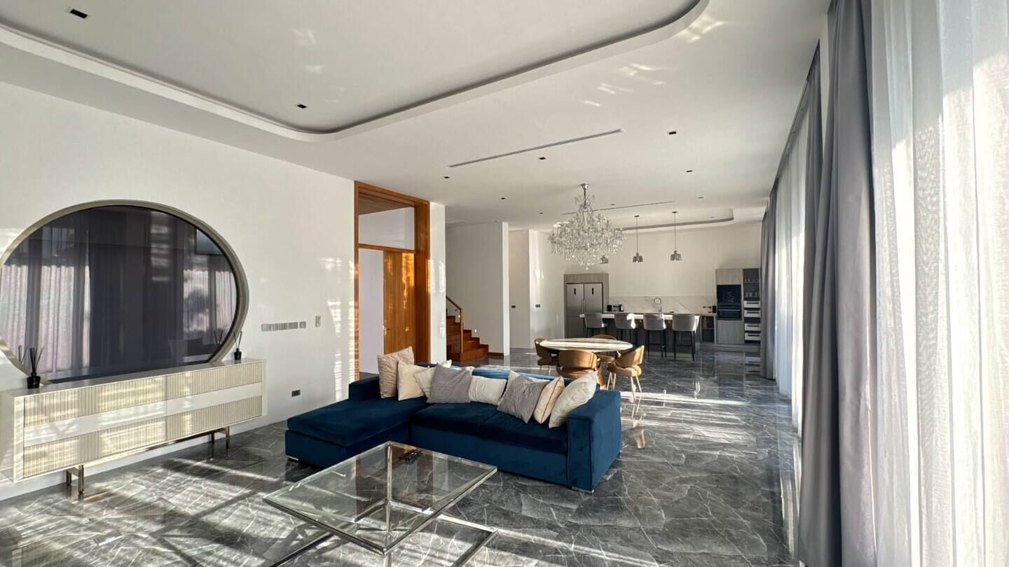 A modern living room with a sectional sofa, a glass coffee table, and a large round mirror.