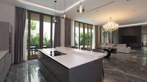 A modern kitchen with a large island, dining area with a table and chairs, and a living room with a sofa and TV.
