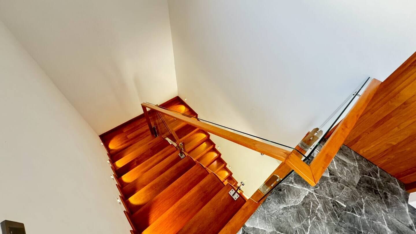 A wooden staircase with a glass handrail leading to a marble floor.