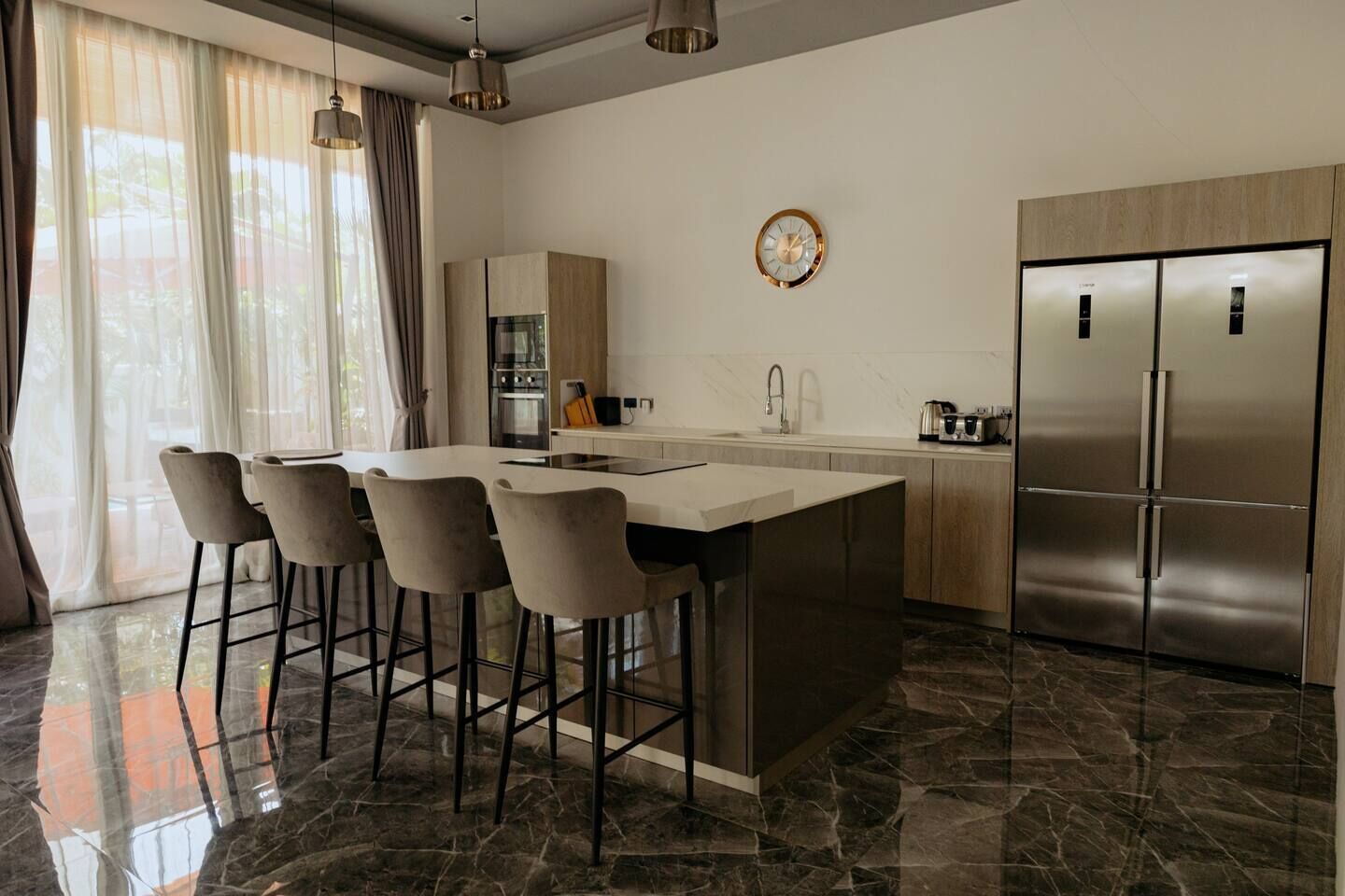 Une cuisine moderne dotée d’un îlot central, de tabourets de bar, d’appareils électroménagers en acier inoxydable et d’une grande fenêtre agrémentée de rideaux.