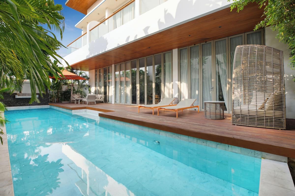 Uma área moderna na piscina com um deck de madeira, espreguiçadeiras e uma ampla parede envidraçada.