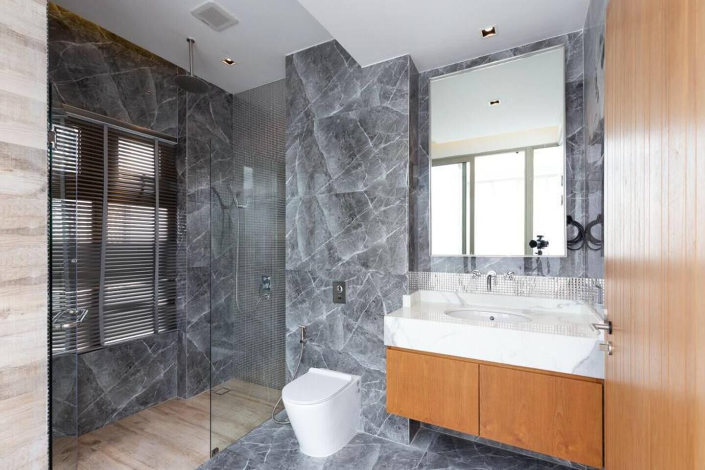 Een moderne badkamer met een douchecabine van glas, marmeren wanden en een houten wastafelmeubel met een grote spiegel.