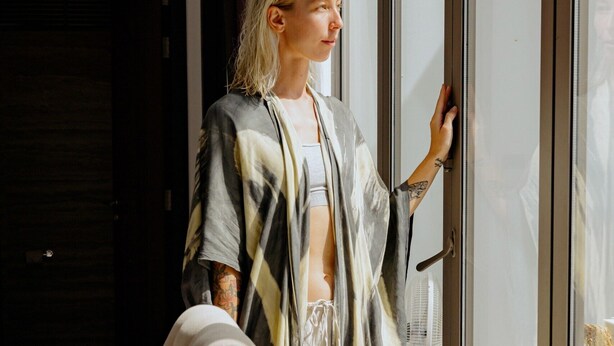 A person standing by a glass door in a modern room with a dark wooden door and a white floor.