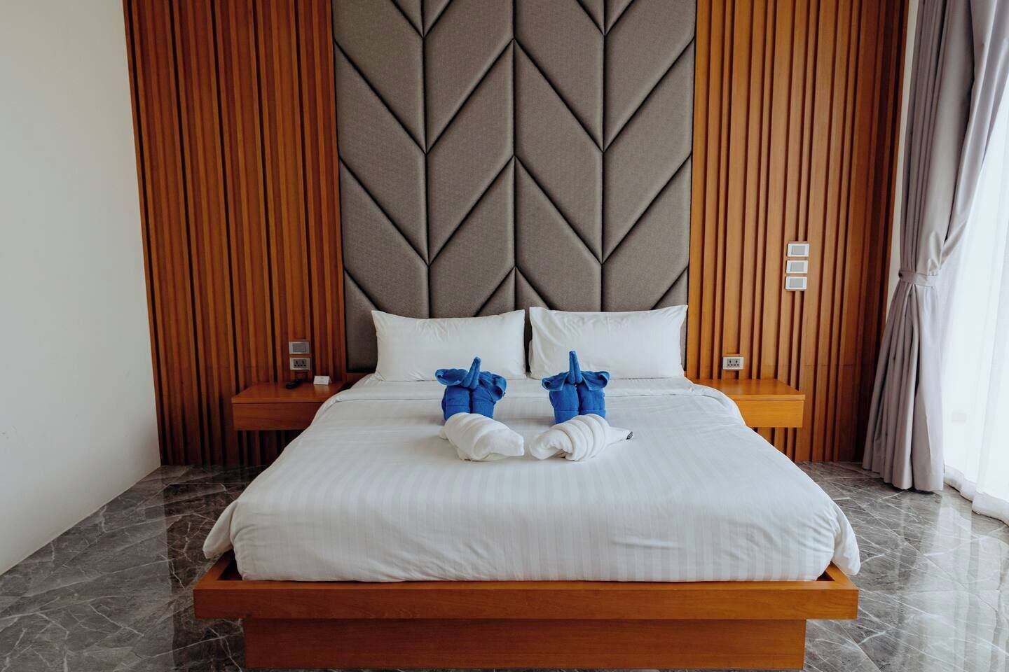 A modern hotel room with a large bed, wooden headboard, and a marble floor.