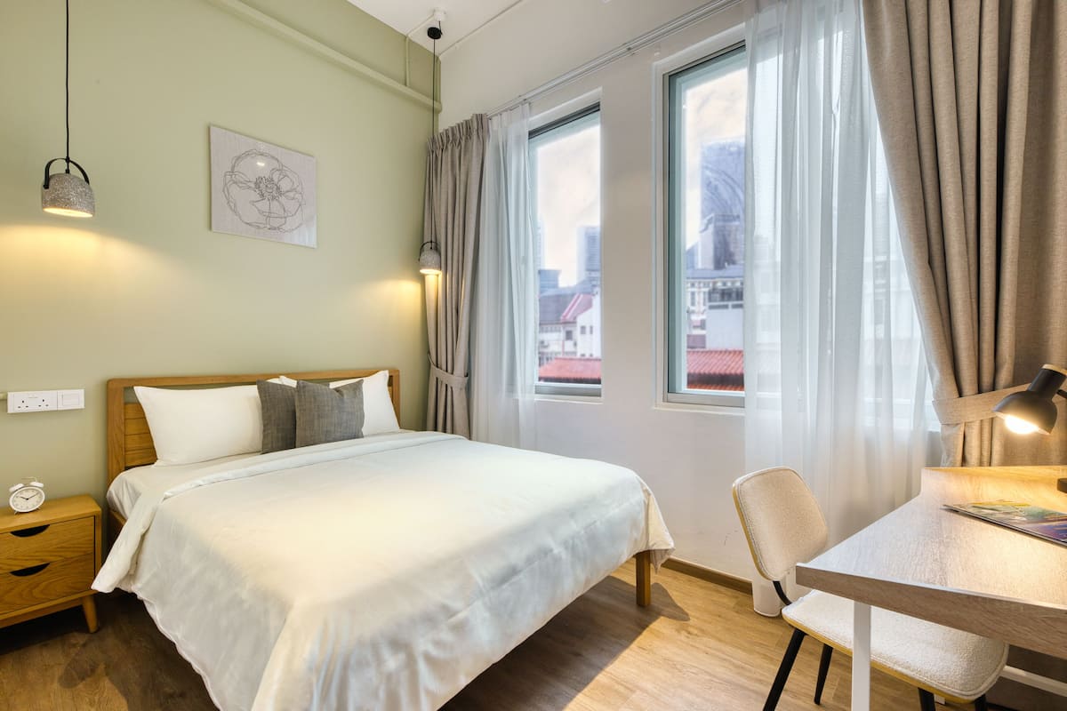 A neatly arranged bedroom with a bed, bedside table, lamp, and a view of the outside through a window.