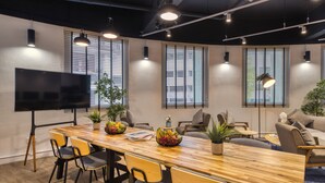 A modern meeting room with a long wooden table, comfortable seating, potted plants, and large windows with blinds. - Hmlet Kada at Maxwell (Singapore)