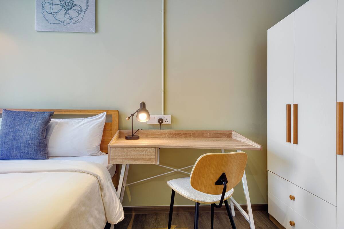 A bedroom with a bed, a desk with a chair, a lamp, and a wardrobe.