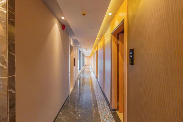A hotel hallway with marble flooring, wooden doors, and a patterned tile border.