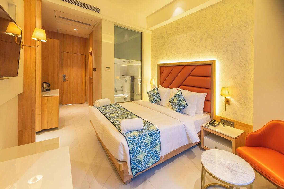 Een hotelkamer met een groot bed, een nachtkastje, een stoel en een badkamer zichtbaar door een geopende deur.