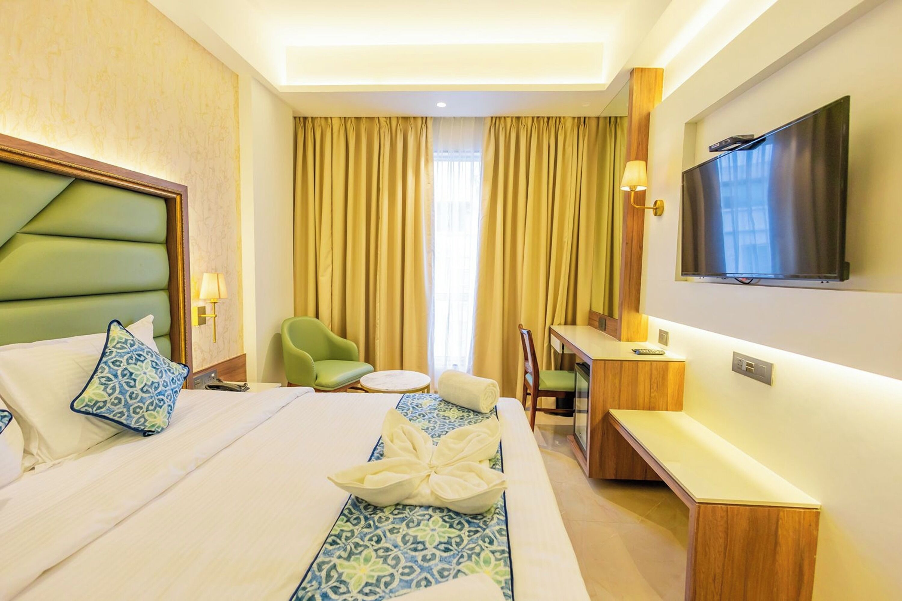 Een hotelkamer met een bed, bureau, stoel, televisie en een raam met gordijnen.