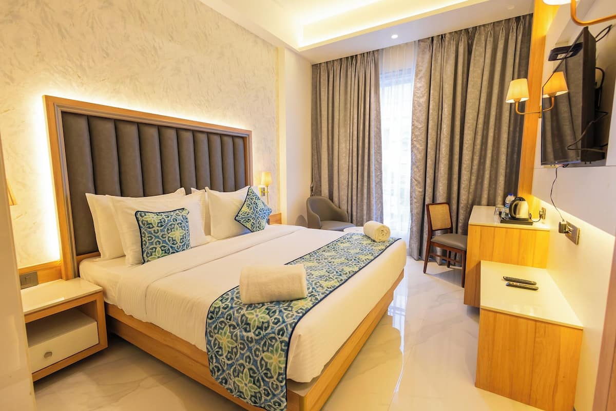 Een hotelkamer met een groot bed, nachtkastje, bureau, stoel, televisie en een raam met gordijnen.