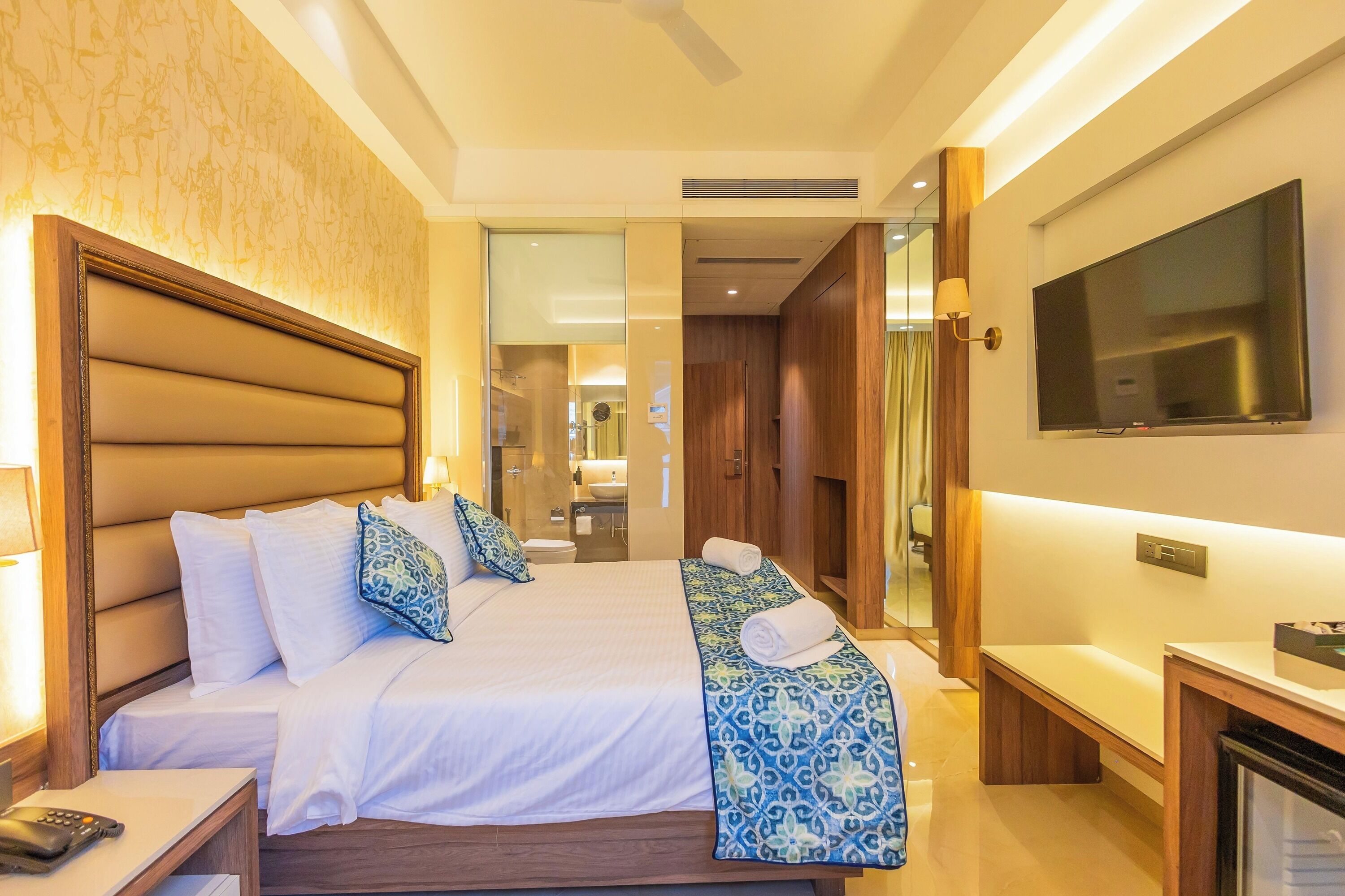 A hotel room with a large bed, bedside tables, a TV, and a bathroom visible through an open door.