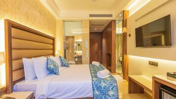 A hotel room with a large bed, bedside tables, a TV, and a bathroom visible through an open door.