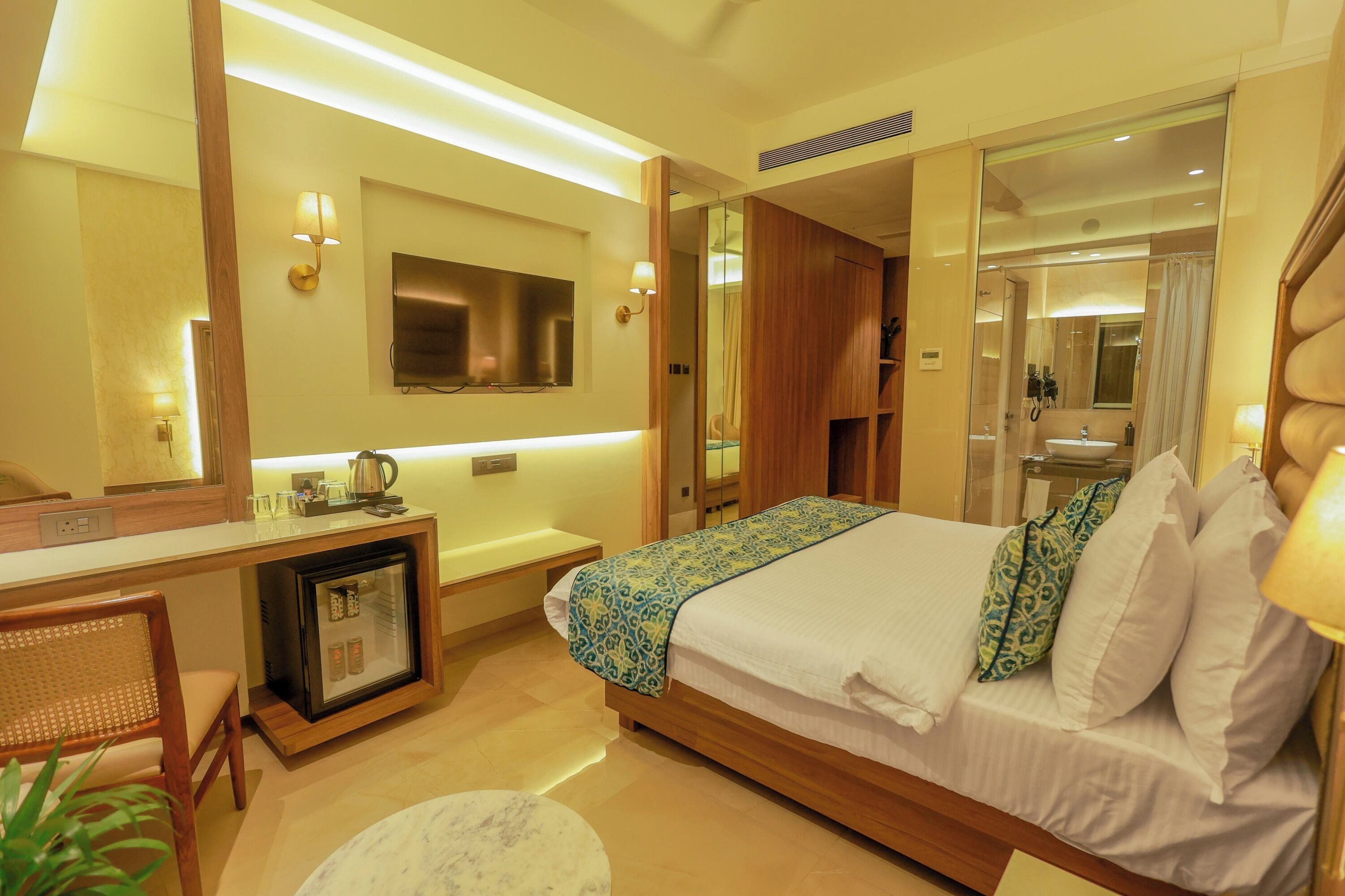 Habitación de hotel con cama, mesita de noche, escritorio con refrigerador y espejo.