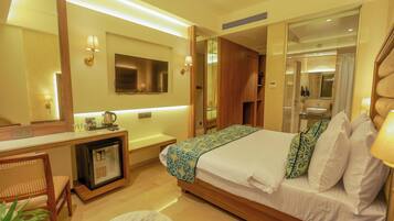 Habitación de hotel con cama, mesita de noche, escritorio con refrigerador y espejo.