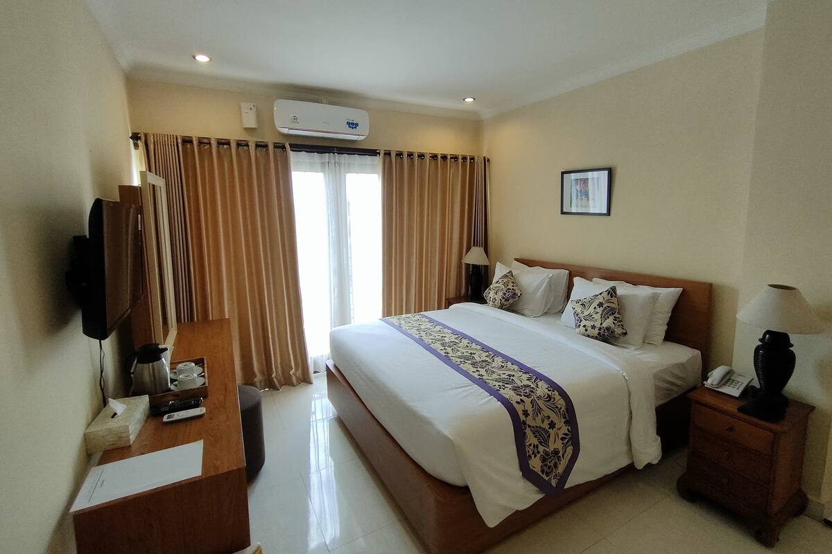 A hotel room with a bed, a desk, a television, a telephone, and a window with curtains.