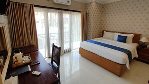 Habitación de hotel con cama, escritorio con silla, ventana con cortinas y un equipo de aire acondicionado en la pared.