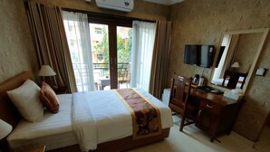 Habitación de hotel con cama, escritorio, silla, televisor y ventana con cortinas.
