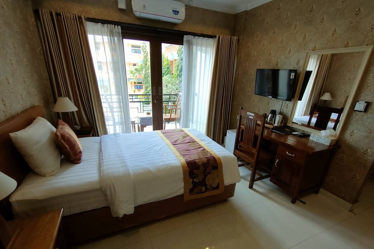 A hotel room with a bed, a desk, a chair, a TV, and a window with curtains.
