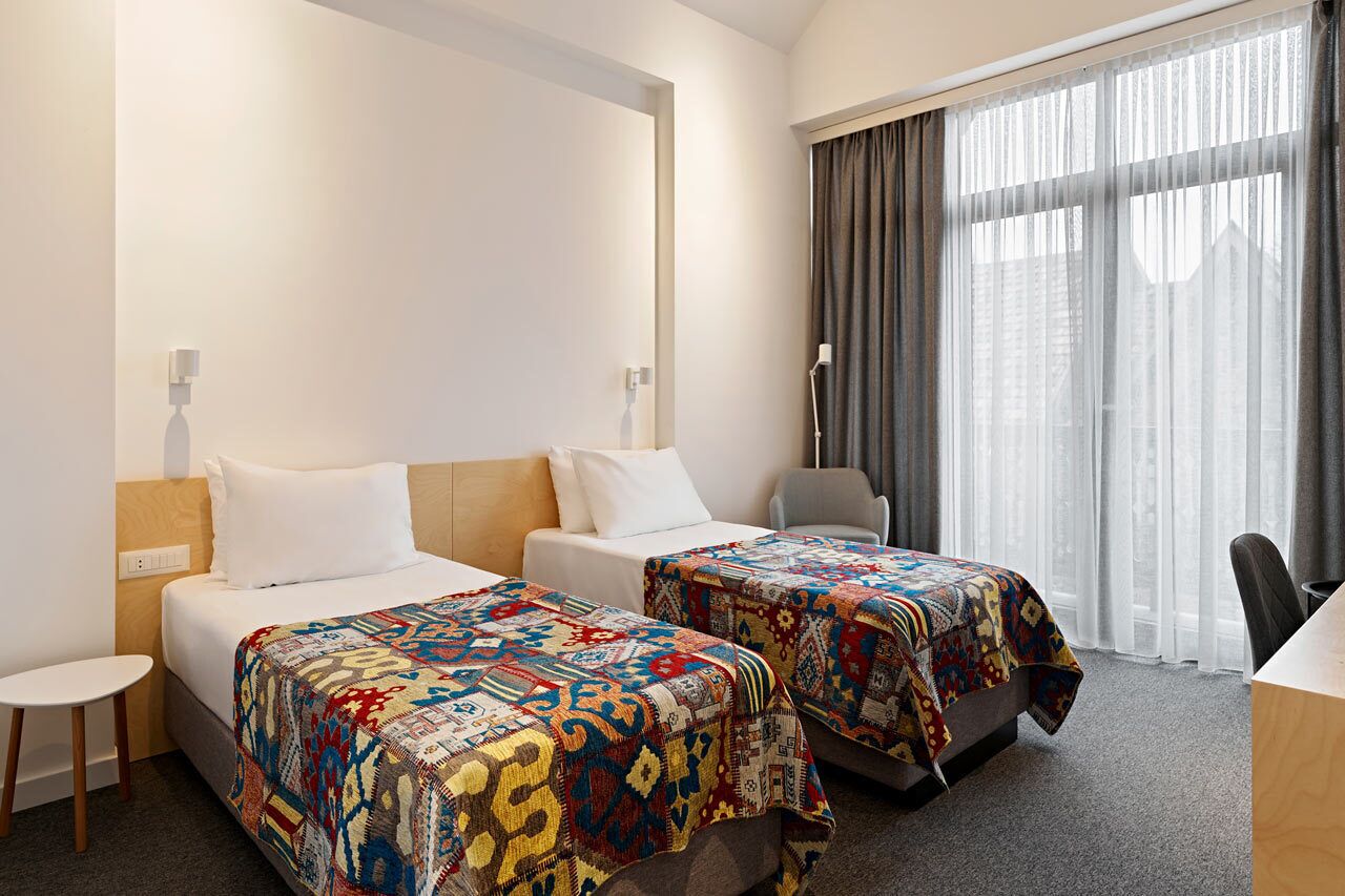Une chambre d’hôtel avec deux lits, un bureau, une chaise et une grande fenêtre avec des rideaux.