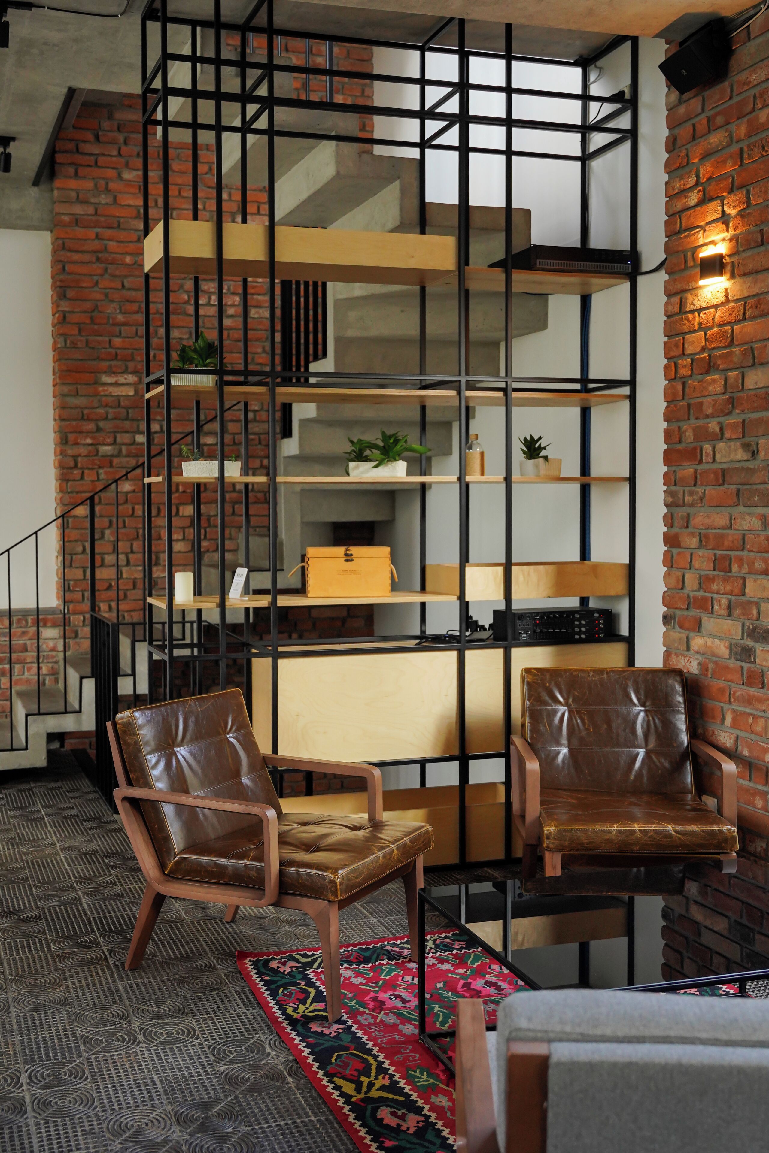 A modern living room with a brick wall, a staircase, and a bookshelf.