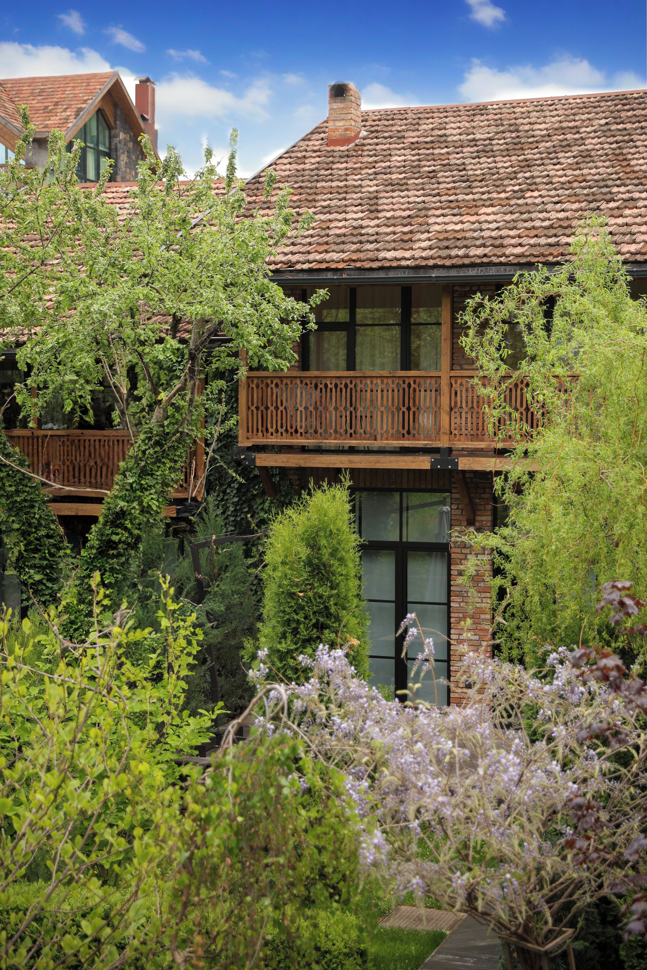 Una casa con tejado de tejas, balcón de madera y un jardín exuberante.