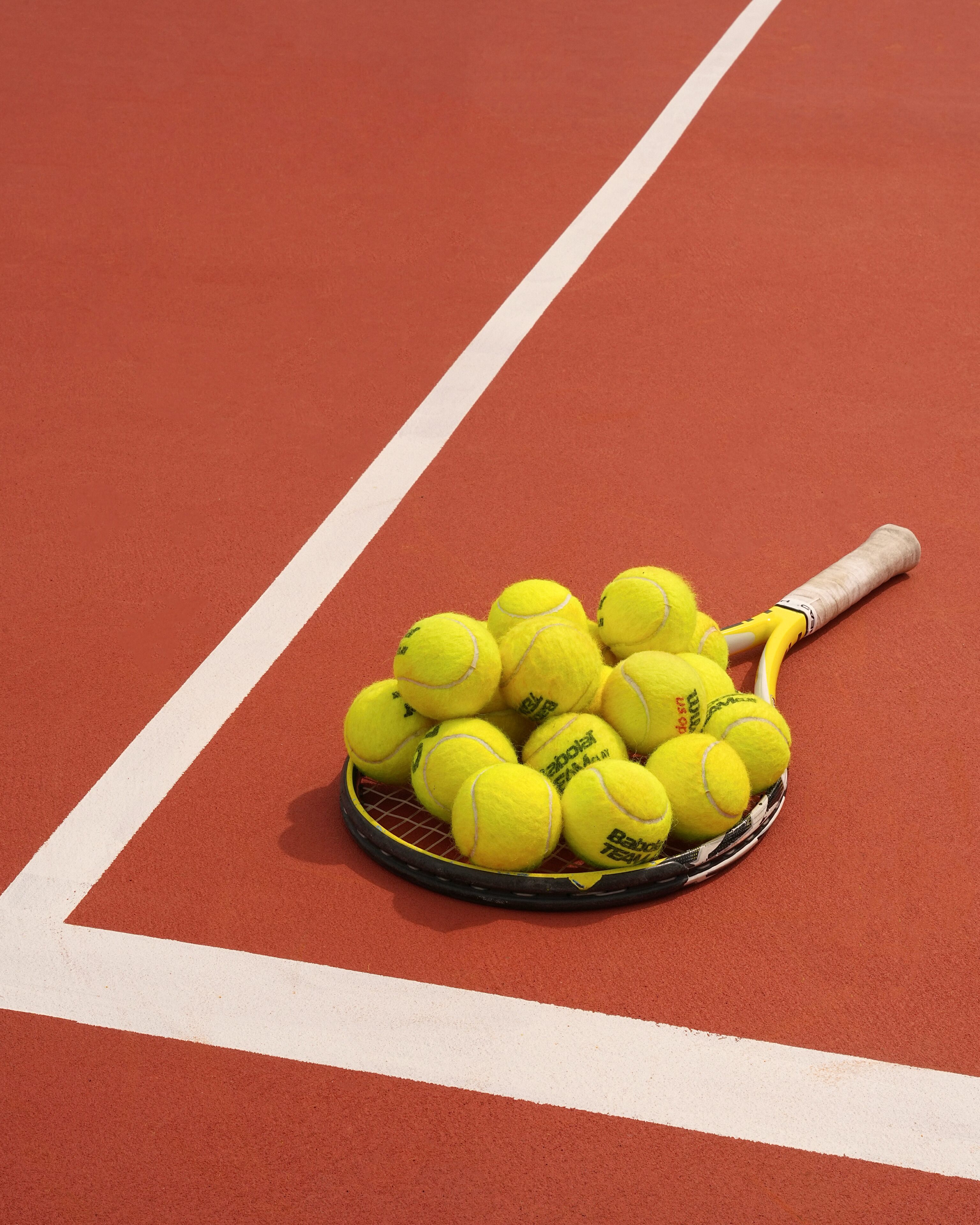Ein Tennisracket mit einem Korb voller gelber Tennisbälle auf einem roten Platz.