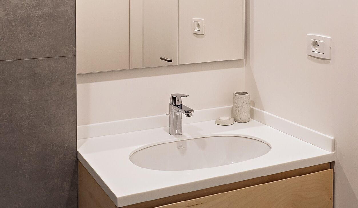 A bathroom with a white sink, a chrome faucet, a mirror, and a toilet paper holder.