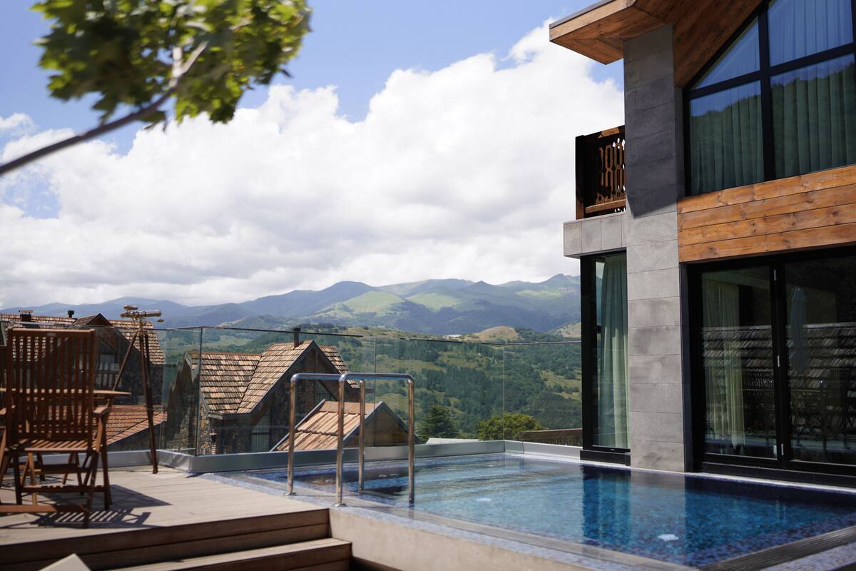 Ein modernes Gebäude mit Schwimmbad, Holzterrasse und Blick auf die Berge.