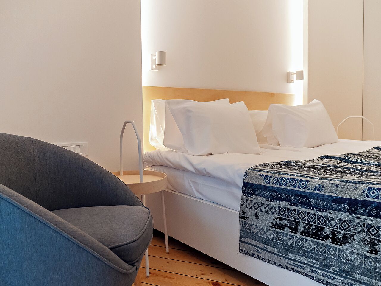 Ein modernes Hotelzimmer mit Bett, Nachttisch, Sessel und Wandleuchte.