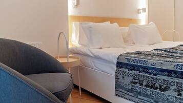 Una habitación de hotel moderna con cama, mesita de noche, una silla y una lámpara fijada a la pared.